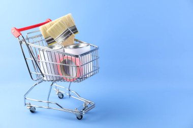 Açık mavi arka planda boya aletleri olan küçük bir alışveriş arabası. Metin için boşluk