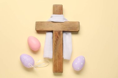 Ahşap haç, beyaz bez ve bej arka planda boyanmış Paskalya yumurtaları.