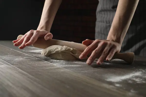 Making bread. Woman rolling dough at wooden table indoors, closeup