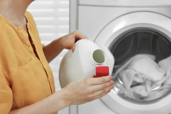 Woman pouring laundry detergent into cap near washing machine indoors, closeup. Space for text