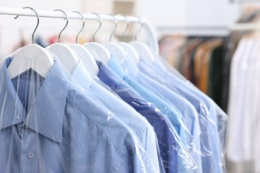 Kuru temizleme servisi. Plastik poşetlerdeki birçok farklı giysi kapalı yerlerde asılı, yakın plan.