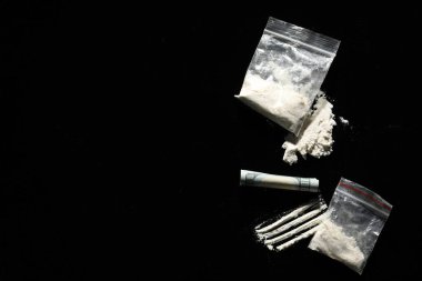 Sert uyuşturuculu plastik torbalar ve siyah arka planda yuvarlanan dolar banknotları. Metin için boşluk