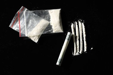 Uyuşturucu bağımlılığı. Kokain dolu plastik torbalar ve siyah arka planda yuvarlanan dolar banknotları.