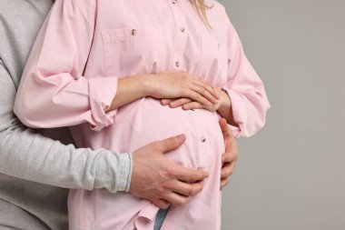 Adam açık gri arka planda hamile eşinin karnına dokunuyor, yakın plan. Metin için boşluk