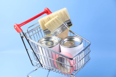 Açık mavi arka planda boyama araçları olan küçük bir alışveriş arabası.