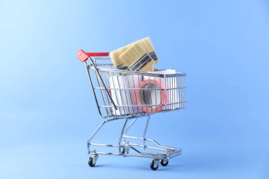 Açık mavi arka planda boyama araçları olan küçük bir alışveriş arabası.