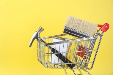 Sarı arka planda boya ve yenileme ekipmanları olan küçük bir alışveriş arabası.