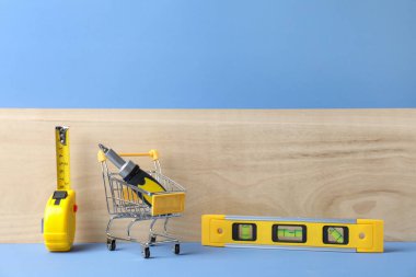 Açık mavi arka planda inşaat aletleri olan küçük bir alışveriş arabası.