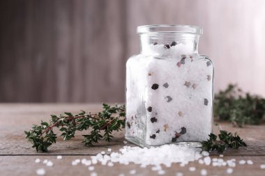 Cam kavanozda biberli tuz ve ahşap masada kekik.