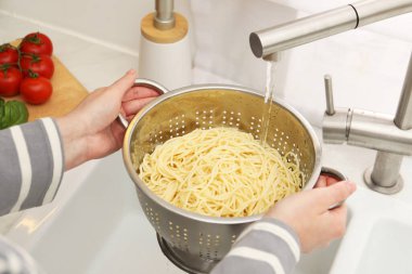 Lavabonun üstünde makarnayı durulayan kadın, yakın plan.