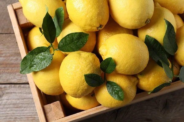 Tahta masadaki sandıkta taze limonlar ve yeşil yapraklar.