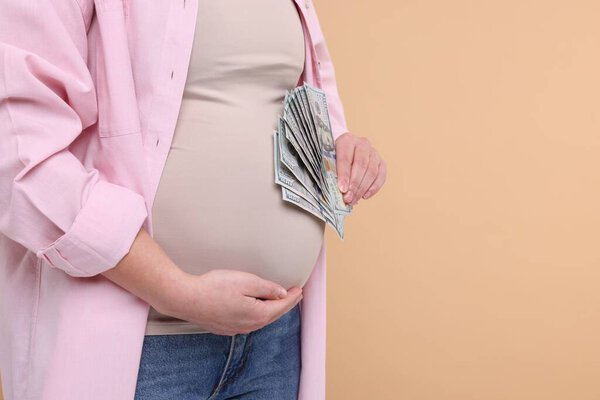 Surrogate mother. Pregnant woman with dollar banknotes on beige background, closeup. Space for text