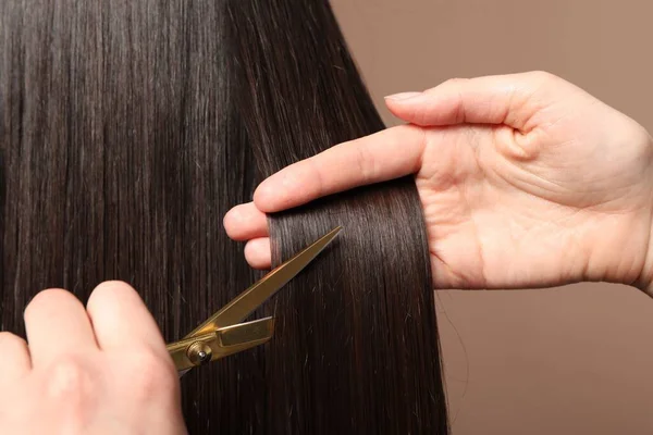 Kuaför açık kahverengi arka planda makasla müşterinin saçını kesiyor.