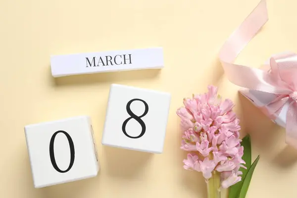 International Women's day - 8th of March. Gift box, wooden block calendar and beautiful flowers on beige background, flat lay