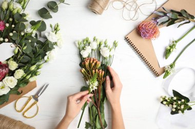 Çiçekçi beyaz ahşap masada güzel bir buket yapıyor.