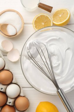 Krem şantili kase, çırpılmış çırpılmış ve malzemeler beyaz ahşap masada, düz yatıyordu.