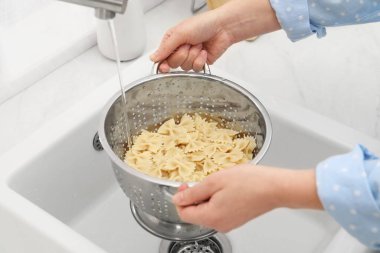 Lavabonun üstünde makarnayı durulayan kadın, yakın plan.