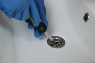 Eldivenli tesisatçı tornavidayla lavaboyu tamir ediyor, yakın plan.