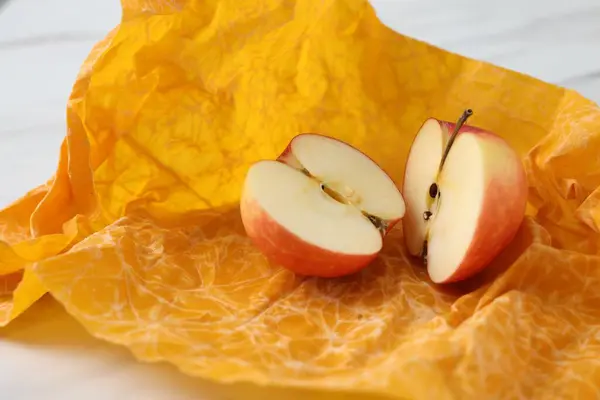 Halves of apple with orange beeswax food wrap on table, closeup