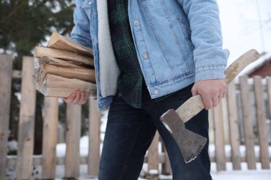 Kış günü baltalı ve odunlu bir adam, yakın plan.