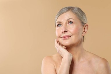 Bej arka planda sağlıklı cildi olan güzel olgun bir kadın.