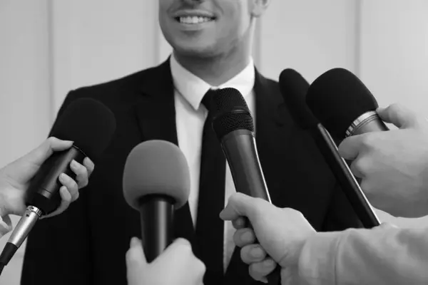 Businessman giving interview to journalists indoors, closeup. Black and white effect