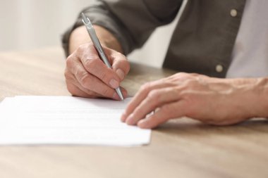 Ahşap masada son arzusunu ve vasiyetini imzalayan kıdemli adam, yakın plan.