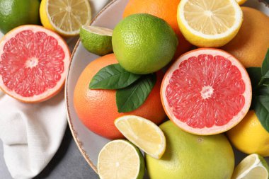 Farklı taze turunçgiller ve yapraklar gri masada, üst tarafta.