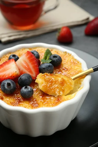 Gri masadaki kaseden alınan meyvelerle nefis bir creme brulee, yakın plan.