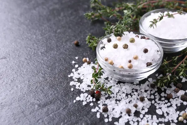 Taze kekikli tuz ve koyu gri desenli masada biber, yakın plan. Metin için boşluk