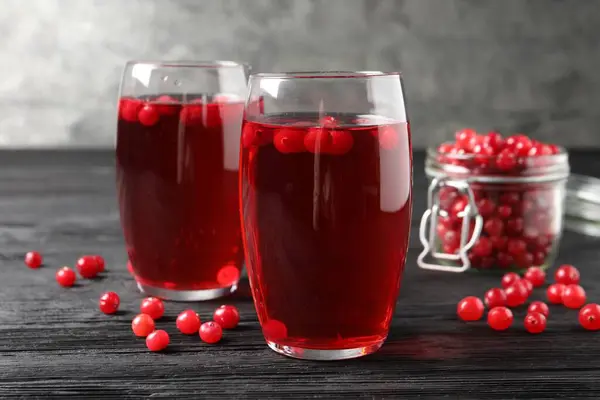 Tasty cranberry juice in glasses and fresh berries on black wooden table, closeup