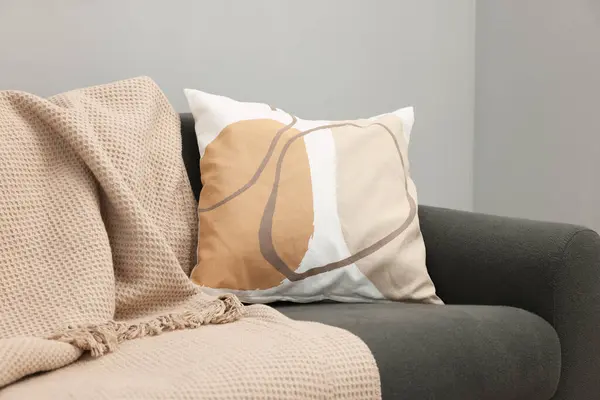 Soft pillow and blanket on sofa near grey wall indoors