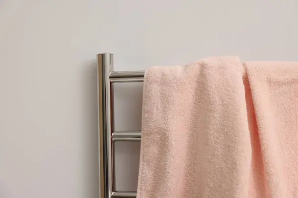 Heated rail with pink towel on white wall, closeup