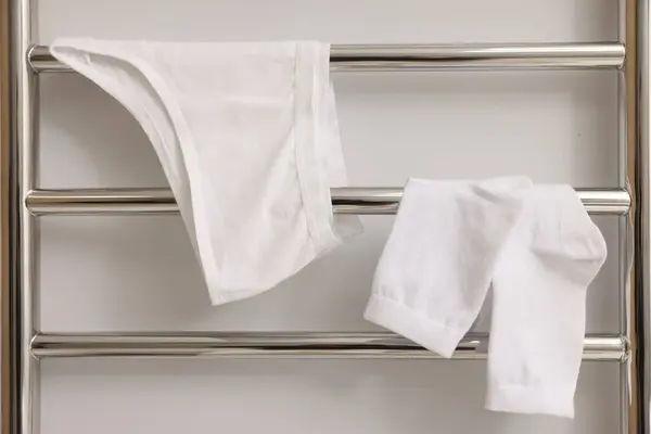 Heated towel rail with underwear and socks on white wall, closeup
