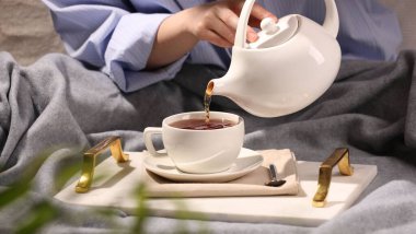 Kadın masadaki fincana aromatik çay dolduruyor, yakın plan.