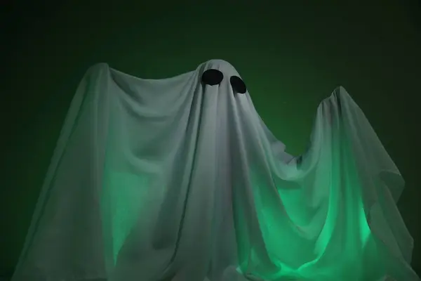 Creepy ghost. Woman covered with sheet in green light, low angle view