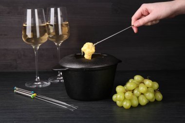 Siyah ahşap masada erimiş peynirle üzümü fondü kabına daldıran kadın, yakın plan.