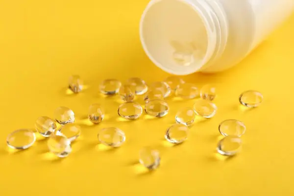 Vitamin capsules and medical bottle on yellow background, closeup