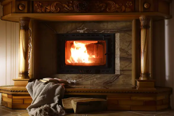Blanket, books and firewood near fireplace at home