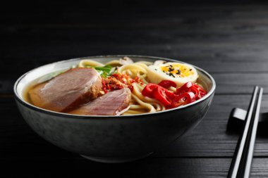 Kasede lezzetli ramen ve siyah ahşap masada çubuklar, yakın plan. Erişte çorbası.