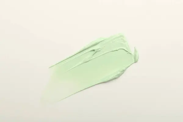 Stroke of green color correcting concealer on white background, top view