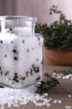 Cam kavanozda biberli tuz ve ahşap masada kekik, yakın plan.