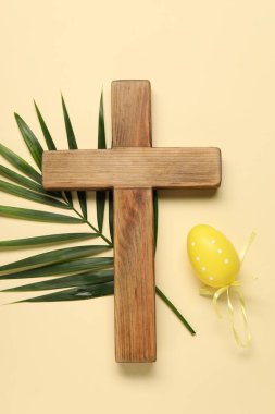 Ahşap haç, boyanmış Paskalya yumurtası ve bej arka planda palmiye yaprağı.