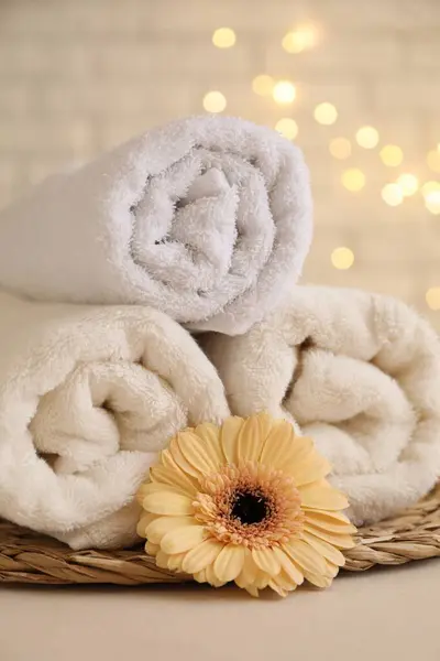 Rolled terry towels and flower on white table near brick wall indoors