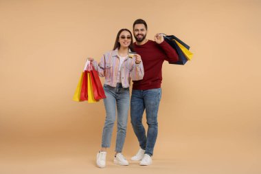 Alışveriş torbalı mutlu çift bej arka planda kredi kartı gösteriyor.