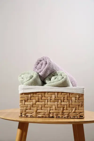 Clean towels in laundry basket on wooden table against gray background, space for text