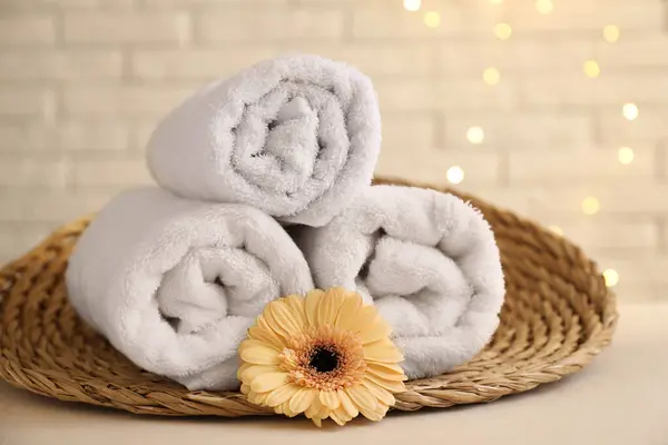 Rolled terry towels and flower on white table near brick wall indoors, closeup
