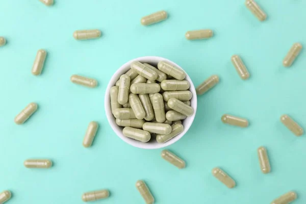 Bowl with vitamin capsules on turquoise background, flat lay