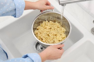 Lavabonun üstünde makarnayı durulayan kadın, yakın plan.