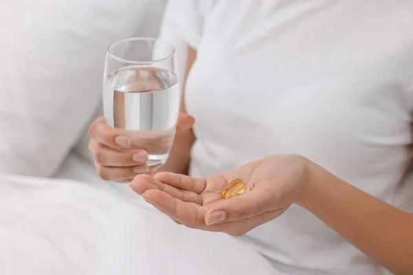 Woman with vitamin pills and glass of water in bed, closeup
